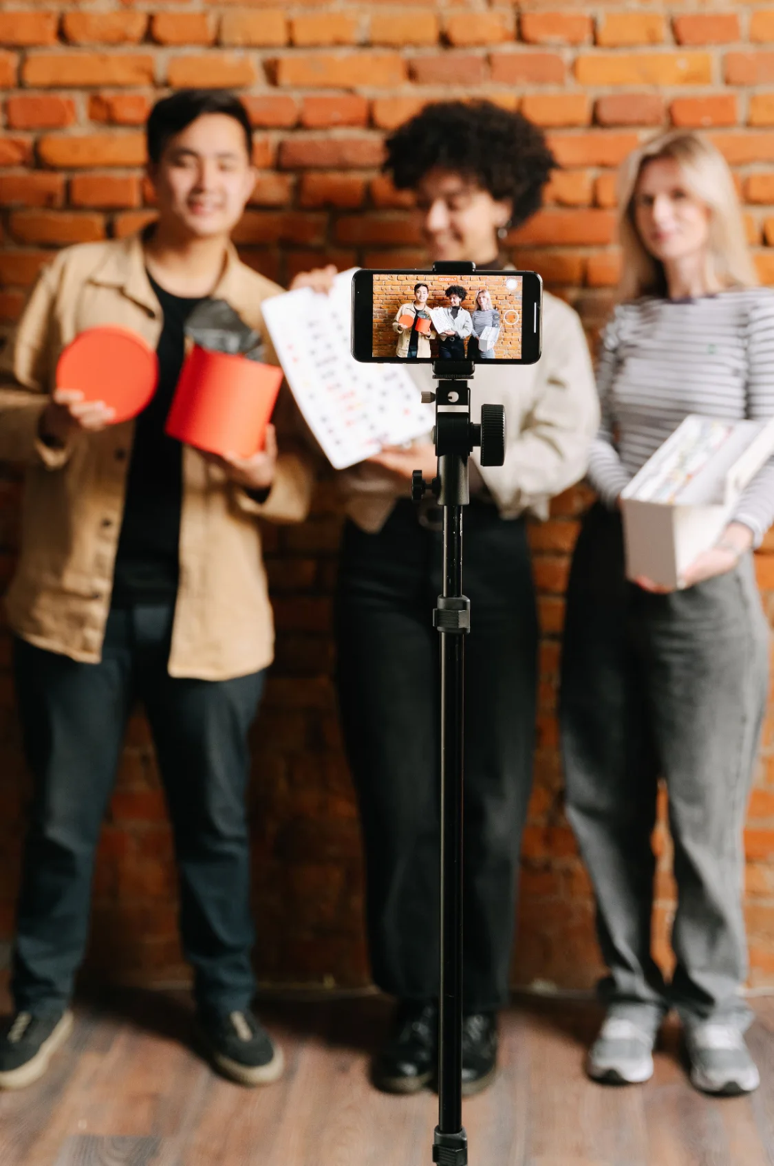 Equipe gravando vídeo para redes sociais com smartphone no tripé em frente a parede de tijolos